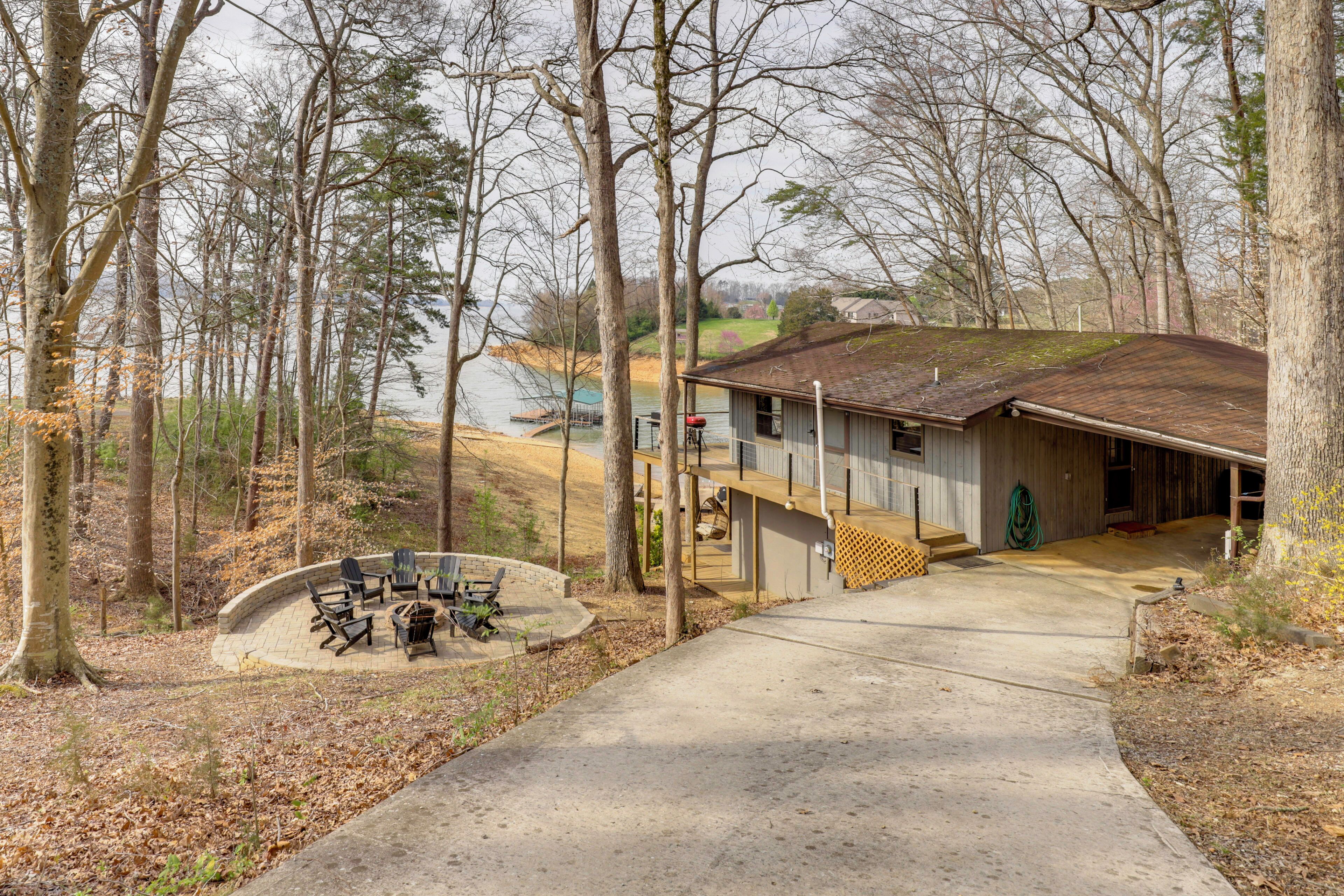 A cabin with a concrete pathway leading to a deck, surrounded by trees and a view of a lake.