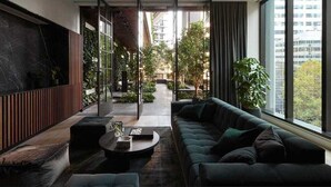 Ein modernes Wohnzimmer mit Sofa, Couchtisch und Blick auf einen Innenhof mit Pflanzen und einem Gebäude im Hintergrund.