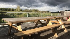 Ett picknickbord i trä står på ett trädäck, med ett metallräcke synligt i bakgrunden.