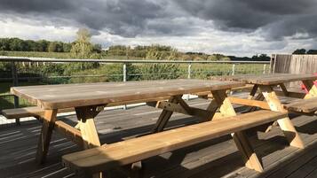 Een houten picknicktafel op een terras met een metalen hekwerk op de achtergrond.