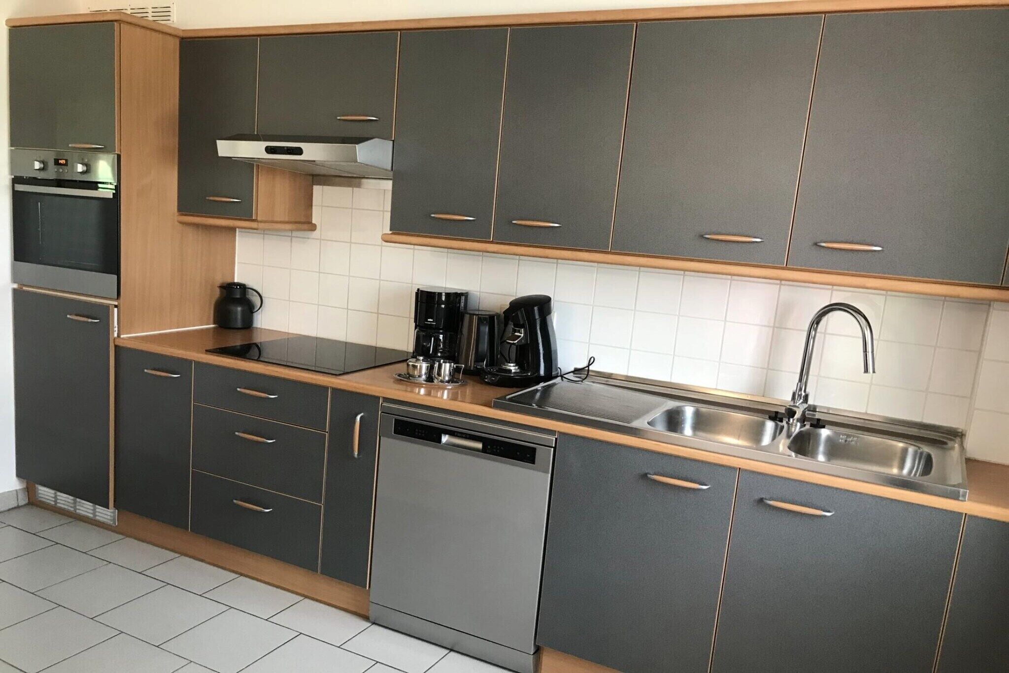 A modern kitchen with grey cabinets, a dishwasher, a coffee maker, and a stainless steel sink.