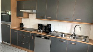 Ett modernt kök med grå skåp, diskmaskin, kaffebryggare och en diskho i rostfritt stål.