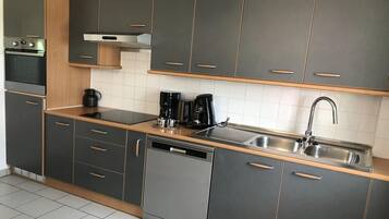 A modern kitchen with grey cabinets, a dishwasher, a coffee maker, and a stainless steel sink.