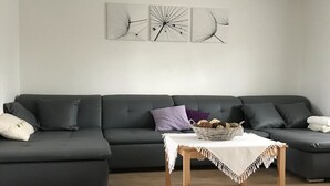 Ett modernt vardagsrum med en mörkgrå hörnsoffa, ett litet träbord med en korg full av bröd och tre abstrakta konstverk på väggen.