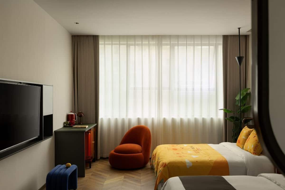 A hotel room with a bed, a chair, a desk, a television, and a window with curtains.