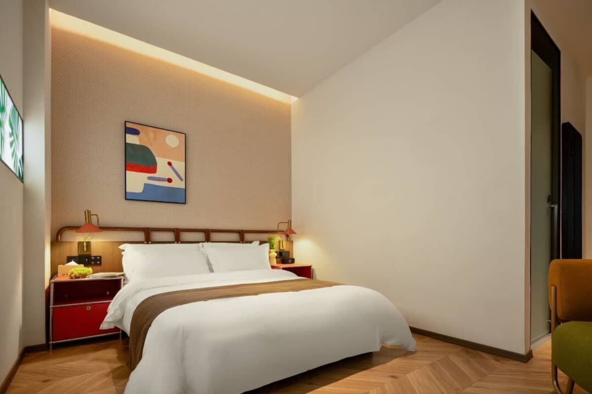 A modern hotel room with a bed, nightstands, a lamp, and a painting on the wall.