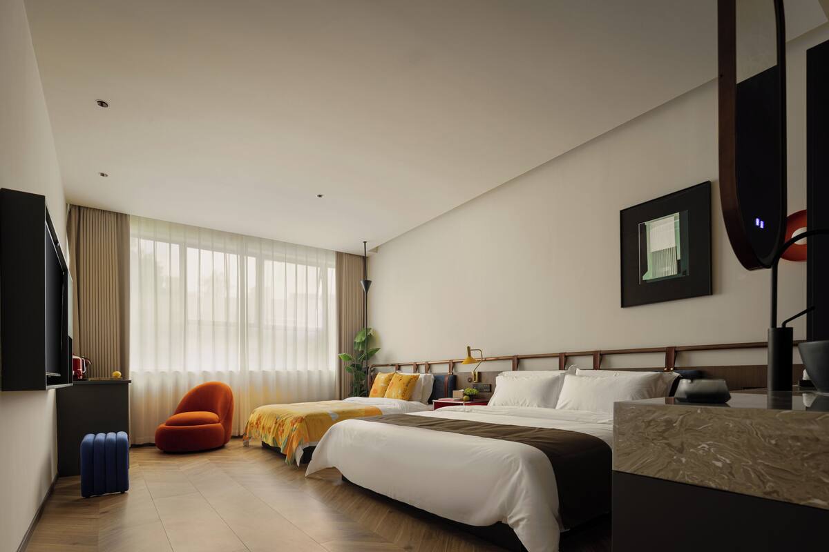 A hotel room with two beds, a desk, a chair, and a large window with curtains.