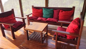 A wooden bench with red cushions and a small table, positioned on a wooden floor with large windows.