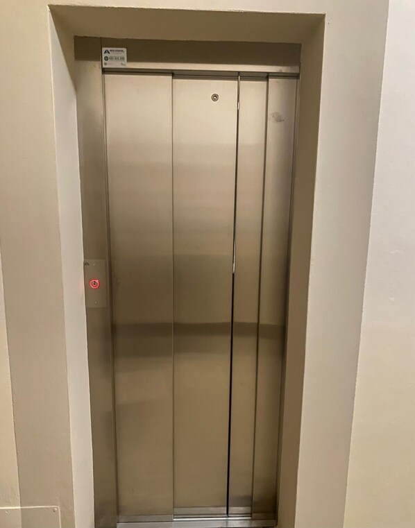 A closed elevator with a metallic finish, a visible emergency stop button, and a sign indicating a fire alarm.