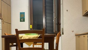 A dining area with a wooden table and chairs, a window with closed blinds, and a tiled floor.