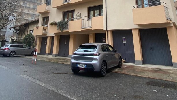 A multi-story residential building with balconies, a parked car, and a gated entrance.