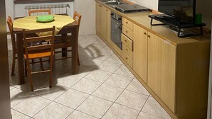A compact kitchen with wooden cabinets, a dining table with chairs, a built-in oven, and a TV on a stand.
