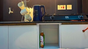 Eine Küchenzeile mit Herd, einer Kaffeemaschine, einem Wandregal für Tassen und einer Flasche Spülmittel.