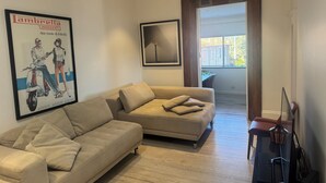 Ein Wohnzimmer mit einem beigefarbenen Sofa, einem gerahmten Bild, einem Holzboden und einer Tür zu einem Außenbereich.