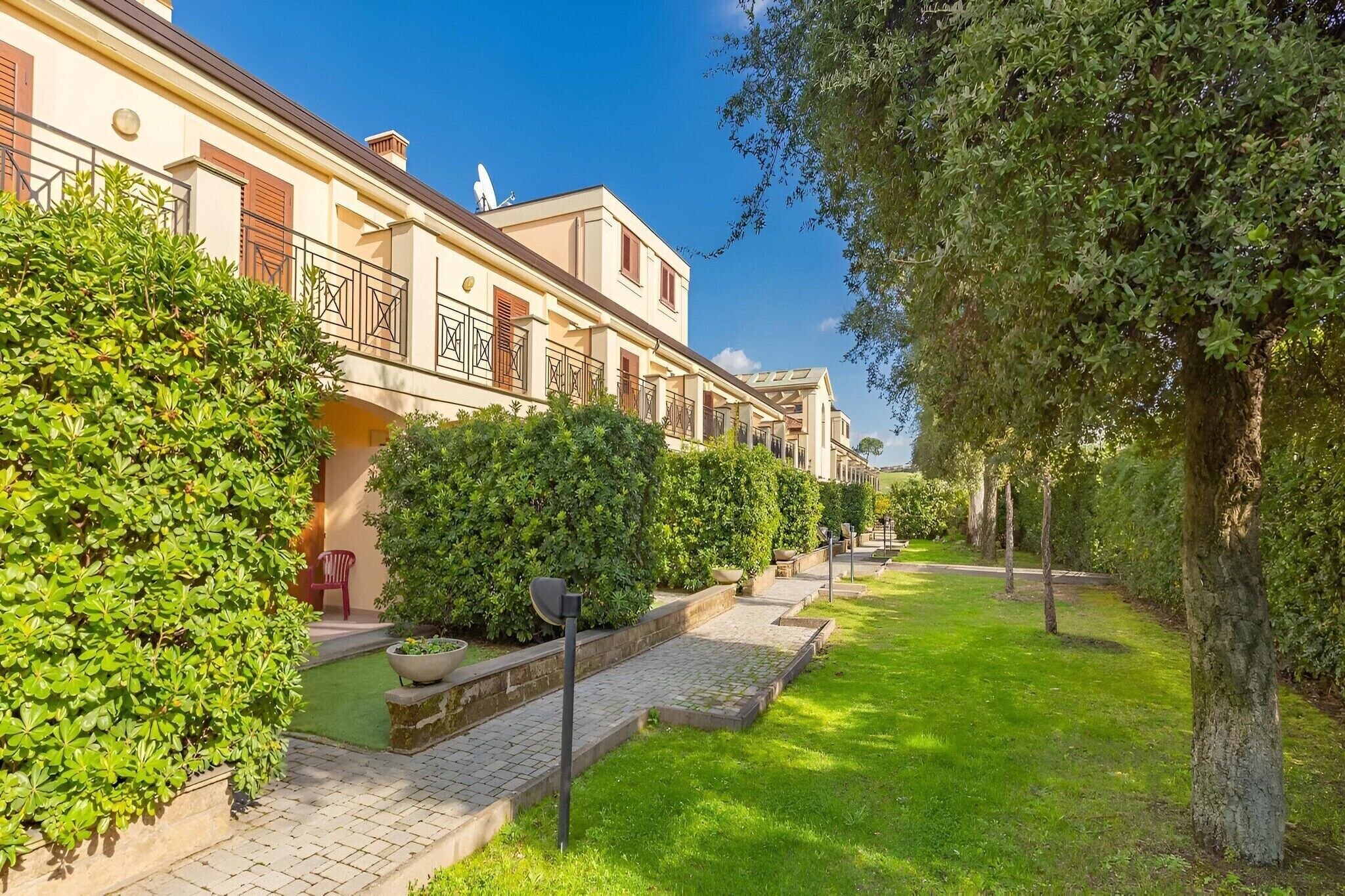 A row of modern buildings with balconies, a paved pathway, and well-maintained greenery.