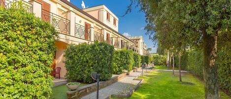 A row of modern buildings with balconies, a paved pathway, and well-maintained greenery.