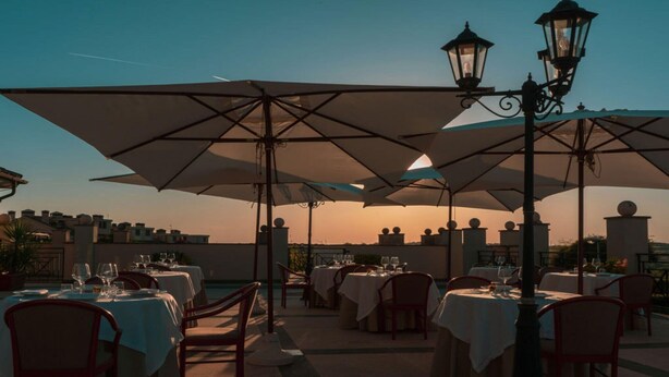 An outdoor dining area with tables, chairs, and umbrellas, set against a sunset backdrop. - Stunning Roman Holiday VIlla for 5 (Roma)