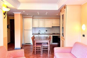 A compact kitchen with white cabinets, a tiled backsplash, and a dining area with a wooden table and chairs. - Roman Base near Marco Simone (Roma)
