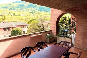 A balcony with a table and chairs, a brick wall, and a view of a green valley with houses. - Bright Holiday Home in Umbria with Pool (Assisi)