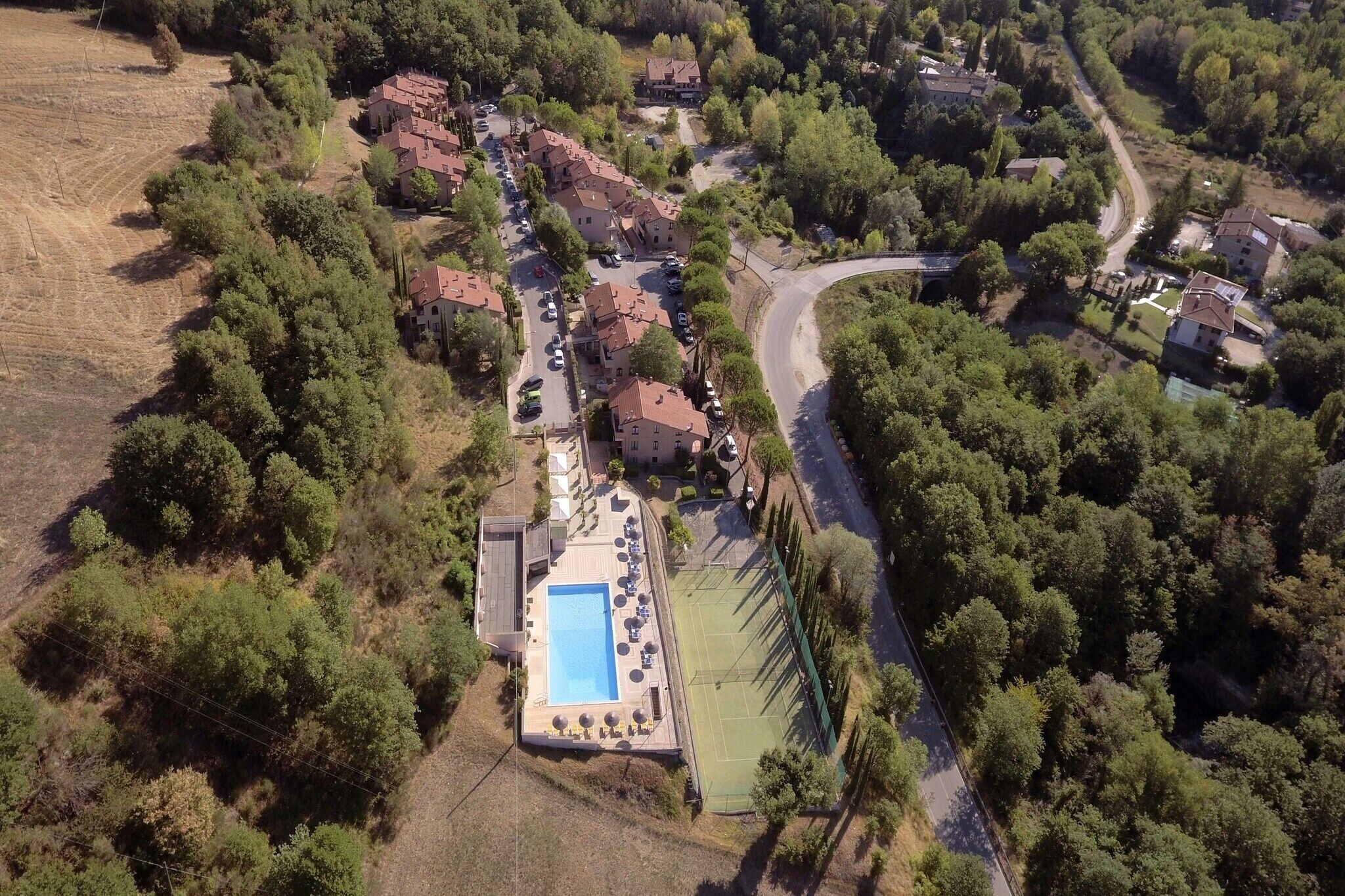 An aerial view of a residential area with houses, a swimming pool, and tennis courts.