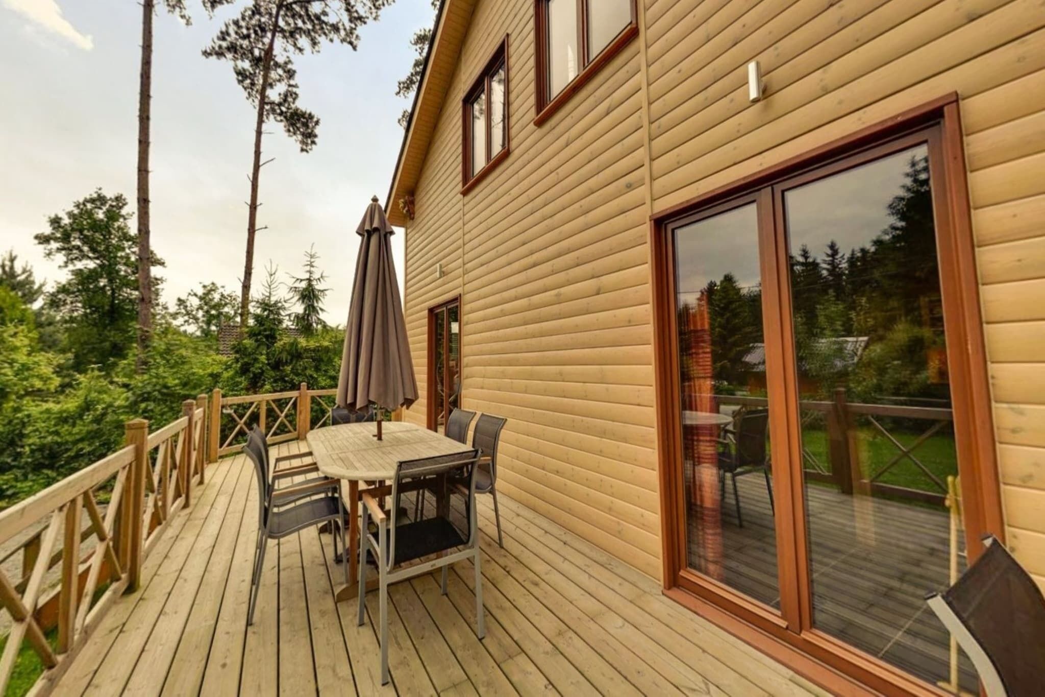 Une terrasse en bois avec une table et des chaises, une grande porte-fenêtre coulissante et une vue sur la verdure environnante.