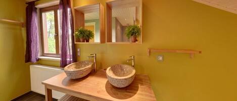 A bathroom with two stone sinks, wooden vanity, mirrors, and potted plants.