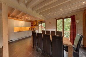 Ein Essbereich mit Holztisch und Stühlen, eine Küche mit weißen Schränken und ein großes Fenster mit Blick auf Grünflächen.