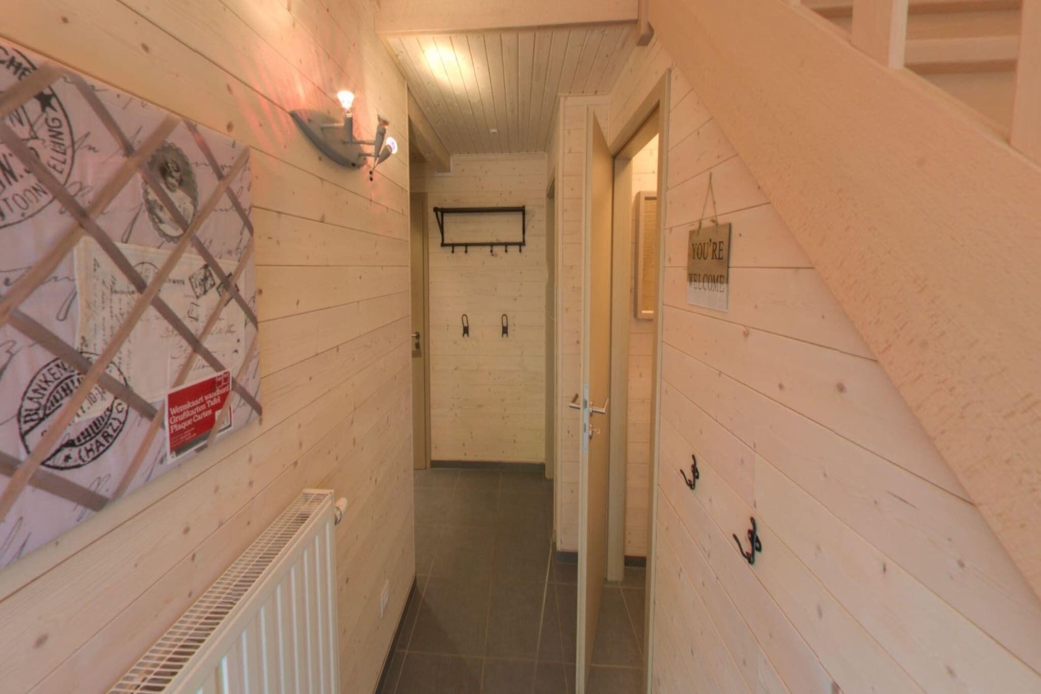 Passadís estret amb parets de fusta, un radiador, una làmpada de paret i una porta amb un senyal.