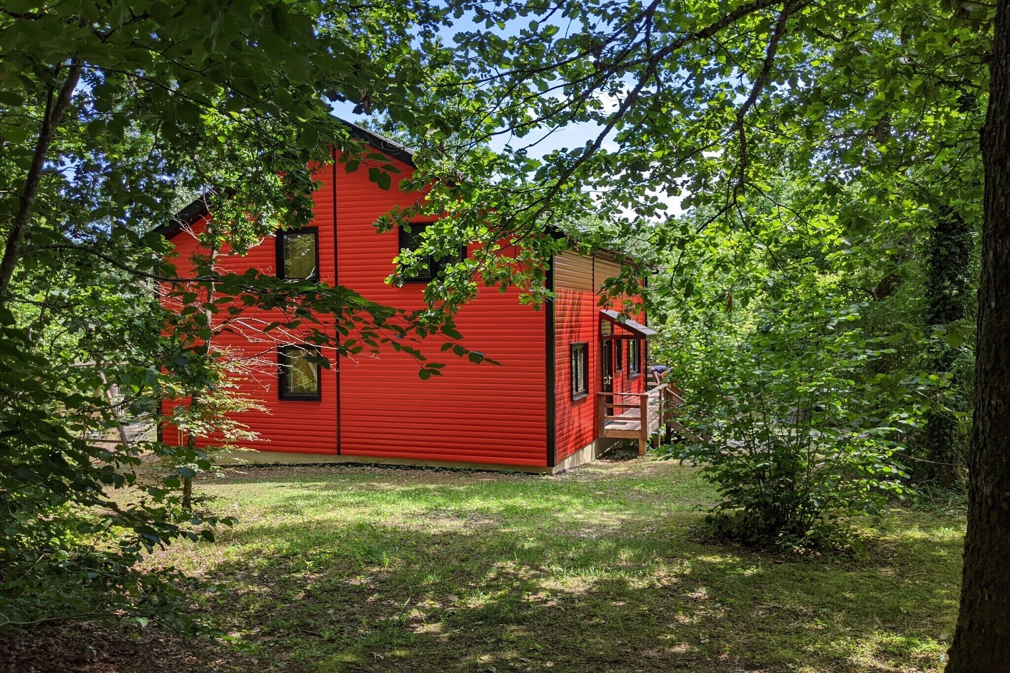 A red wooden cabin with a porch, surrounded by trees.