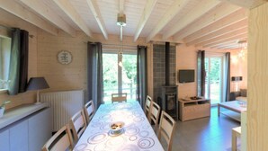 Ein Essbereich mit einem langen Tisch, Stühlen, einem Kamin, einem Fernseher und Blick ins Freie.