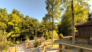 Eine Holzterrasse mit einem Kiesweg, der zu einer rustikalen Holzhütte inmitten dicht bewaldeter Landschaft führt.