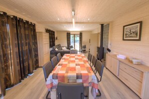 Ein Essbereich mit einem langen Tisch, Stühlen, einer Couch, einem Fernseher und einem Schrank.
