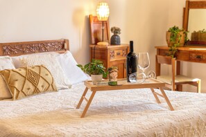 Ein ordentlich bezogenes Bett mit dekorativem Kopfteil, ein Nachttisch mit einer Weinflasche, einem Glas und einer kleinen Topfpflanze.