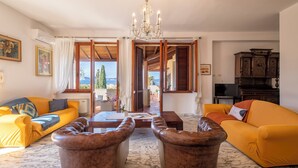 A living room with a yellow sofa, a brown leather ottoman, a wooden coffee table, and a chandelier. - Villa Contessa, a peaceful sea-view retreat (Sardegna)
