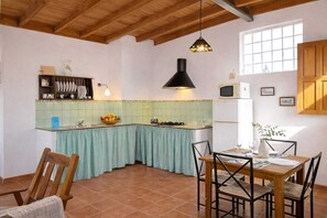 Una cocina con techo de madera, una ventana, un fregadero, una estufa y un comedor con sillas y una mesa.