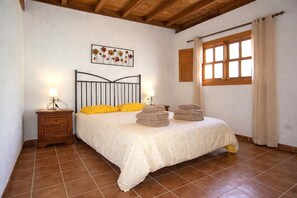 Un dormitorio con cama, mesita de noche, ventana con cortinas e imagen colgada en la pared.