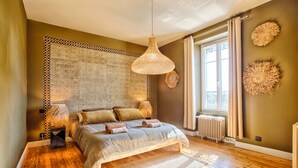 Une chambre à coucher avec un lit, un luminaire suspendu, un radiateur et une fenêtre avec des rideaux.