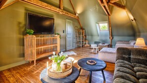 Une pièce de style « loft », avec un plafond en bois, une télévision, un canapé, une petite table et une fenêtre.