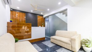 Un espace d’accueil moderne avec un comptoir de réception en bois, un canapé beige, une plante en pot et un ventilateur de plafond.
