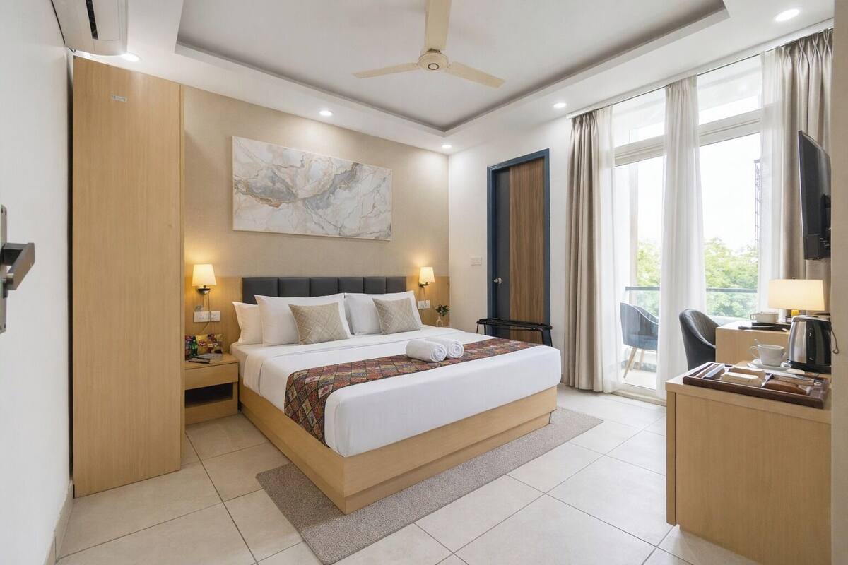A modern hotel room with a large bed, a desk, a television, and a balcony with curtains.