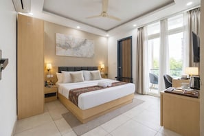 A modern hotel room with a large bed, a desk, a television, and a balcony with curtains. - Fortune Inn Sector - 104 By ASPL (Noida)