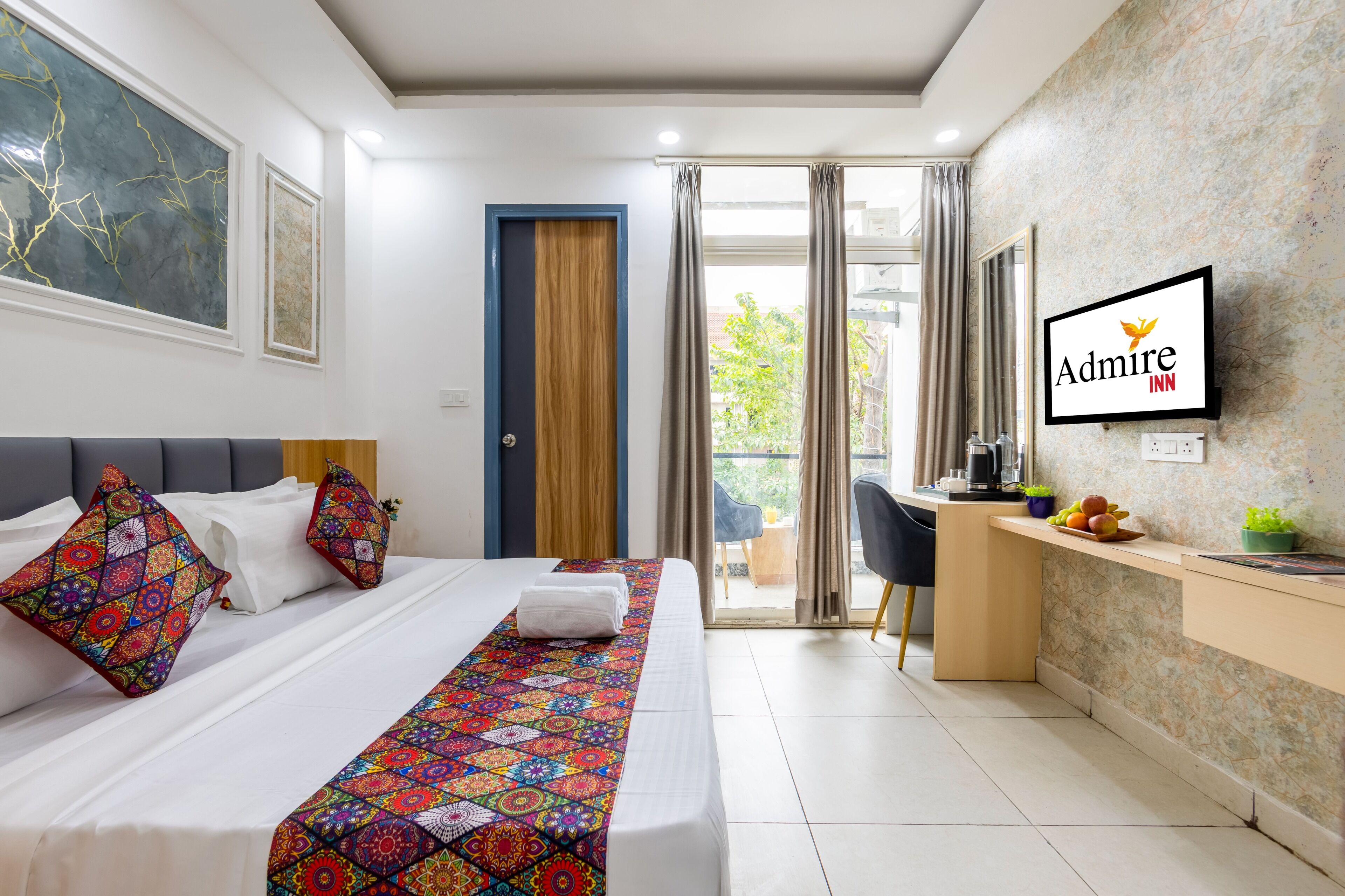 Habitación de hotel con cama, escritorio, silla, televisión y balcón.