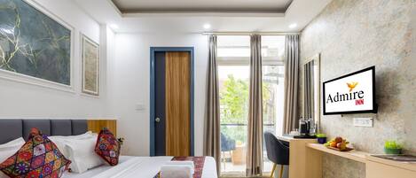 Habitación de hotel con cama, escritorio, silla, televisión y balcón.
