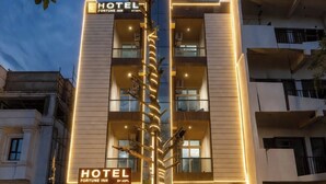 Un hôtel à plusieurs étages, doté d’une entrée imposante, d’une enseigne lumineuse et d’un élément décoratif central.
