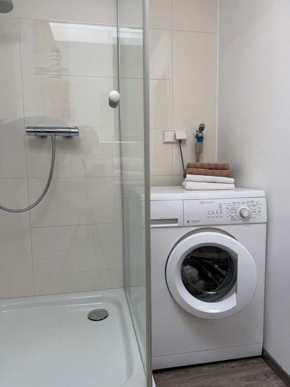 Une salle de bain moderne dotée d’une cabine de douche en verre, d’un lave-linge encastré et d’un porte-serviettes.