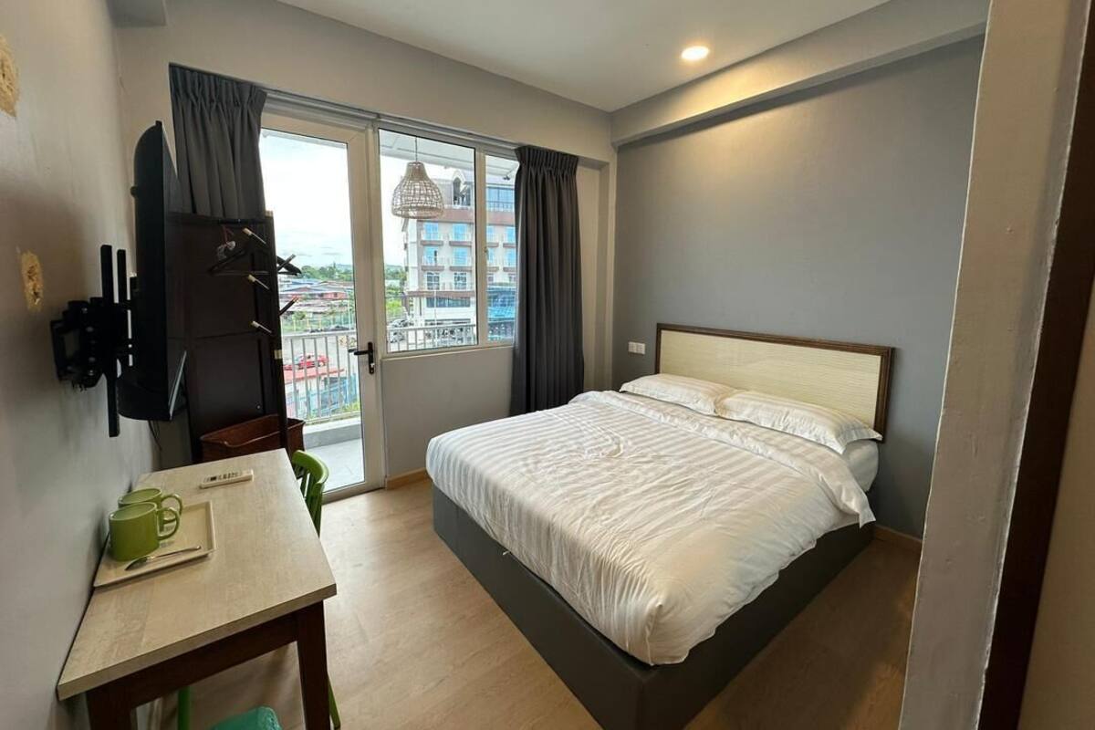Un dormitorio con una cama, un escritorio, una silla, un televisor y una ventana con cortinas.