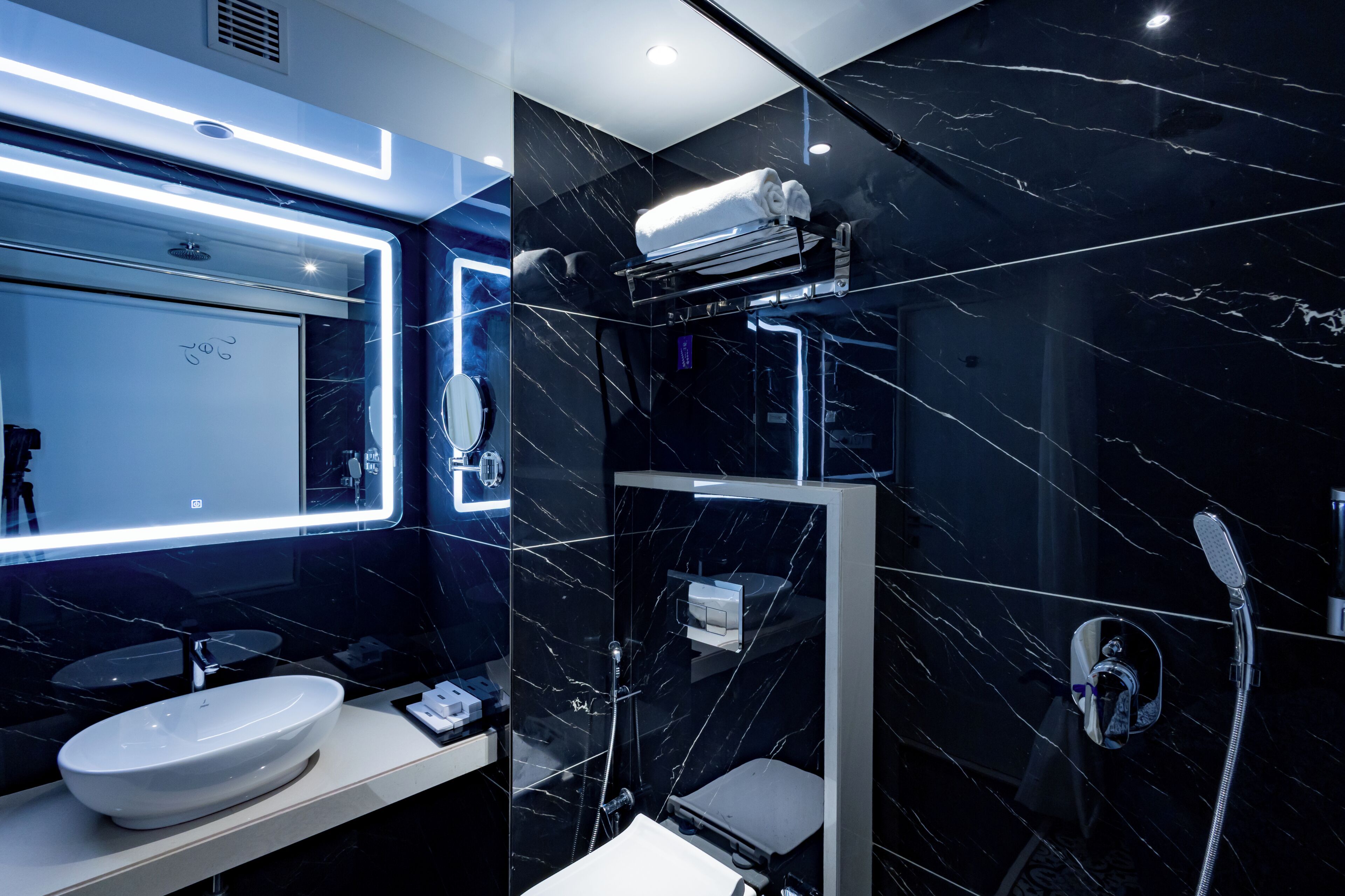 A modern bathroom with a large mirror, a sink, a shower, and a towel rack.