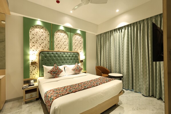 A hotel room with a large bed, a nightstand with a phone, a chair, a small table, and a TV mounted on the wall. - SiO Suites (Navi Mumbai)