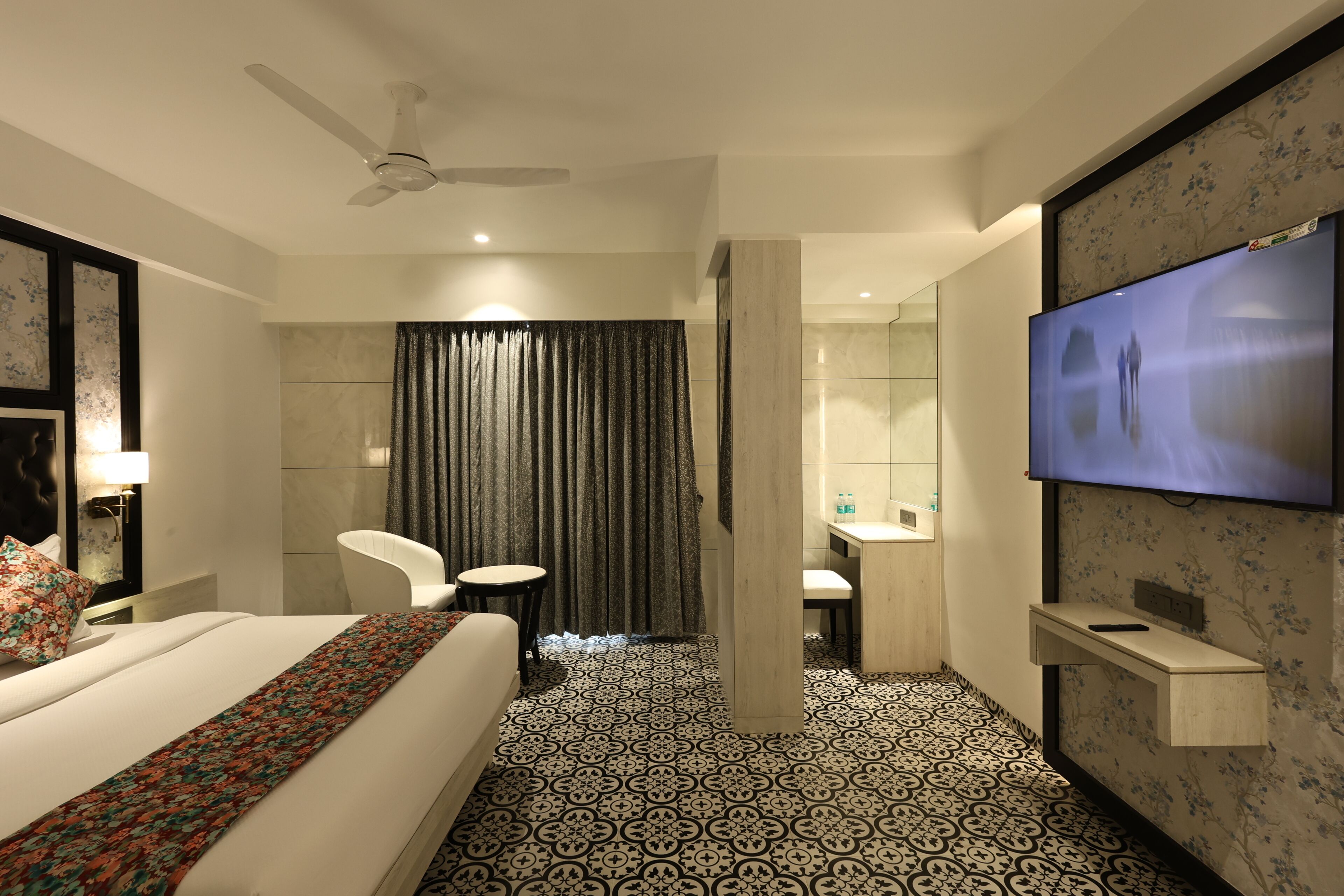 Quarto de hotel com cama, escrivaninha, cadeira, televisão e banheiro.