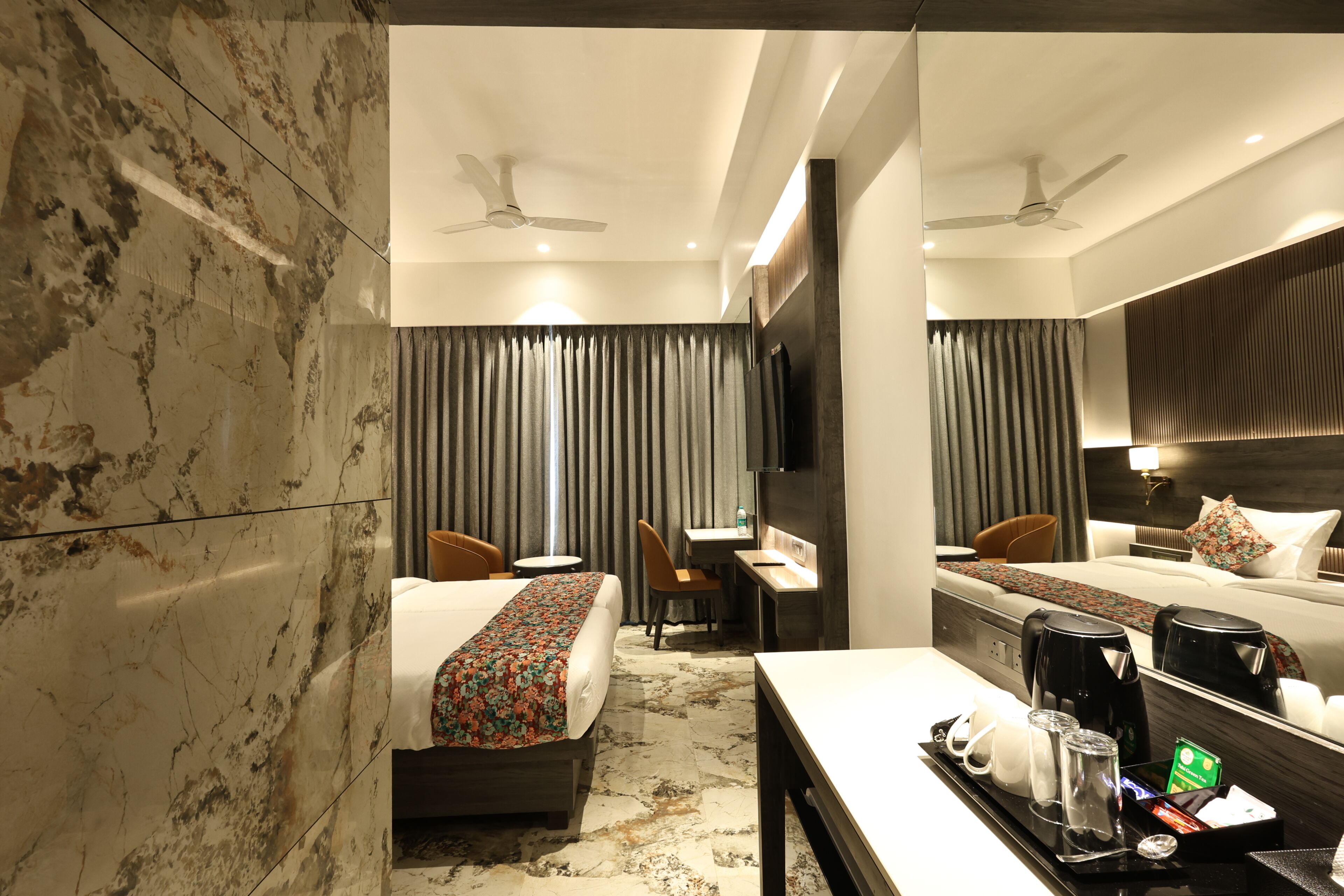 A hotel room with a bed, desk, chairs, a coffee maker, and a tray with cups and glasses.